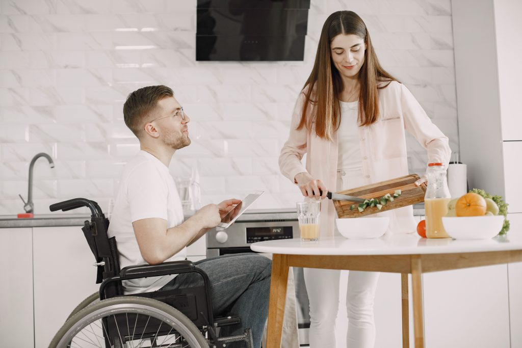 vrouw verzorgt ontbijt bij man in een rolstoel